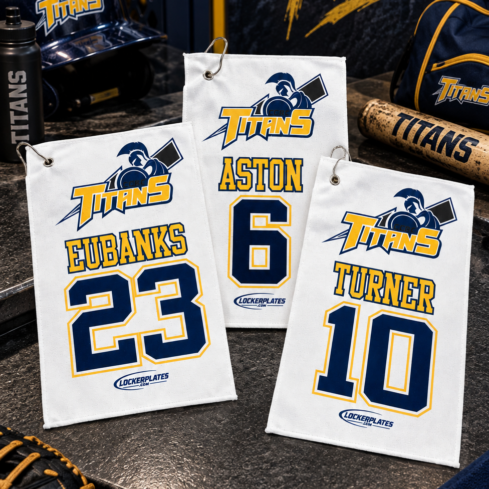Three white baseball-style towel or flag-style accessories with player names and numbers hang on a locker shelf. The towels show the Titans logo and the names Aston 6 and Turner 10, with matching team decor around them including a helmet, baseball, glove, bat, and a sign reading Titan Pride.