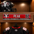 A football helmet and black jersey with red and white accents are displayed inside a wooden locker. A personalized nameplate on the shelf reads PEAK 82 with FAITH ACADEMY FOOTBALL and a ram logo.